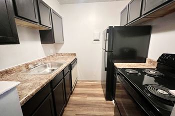 A kitchen with black appliances and wooden floors.